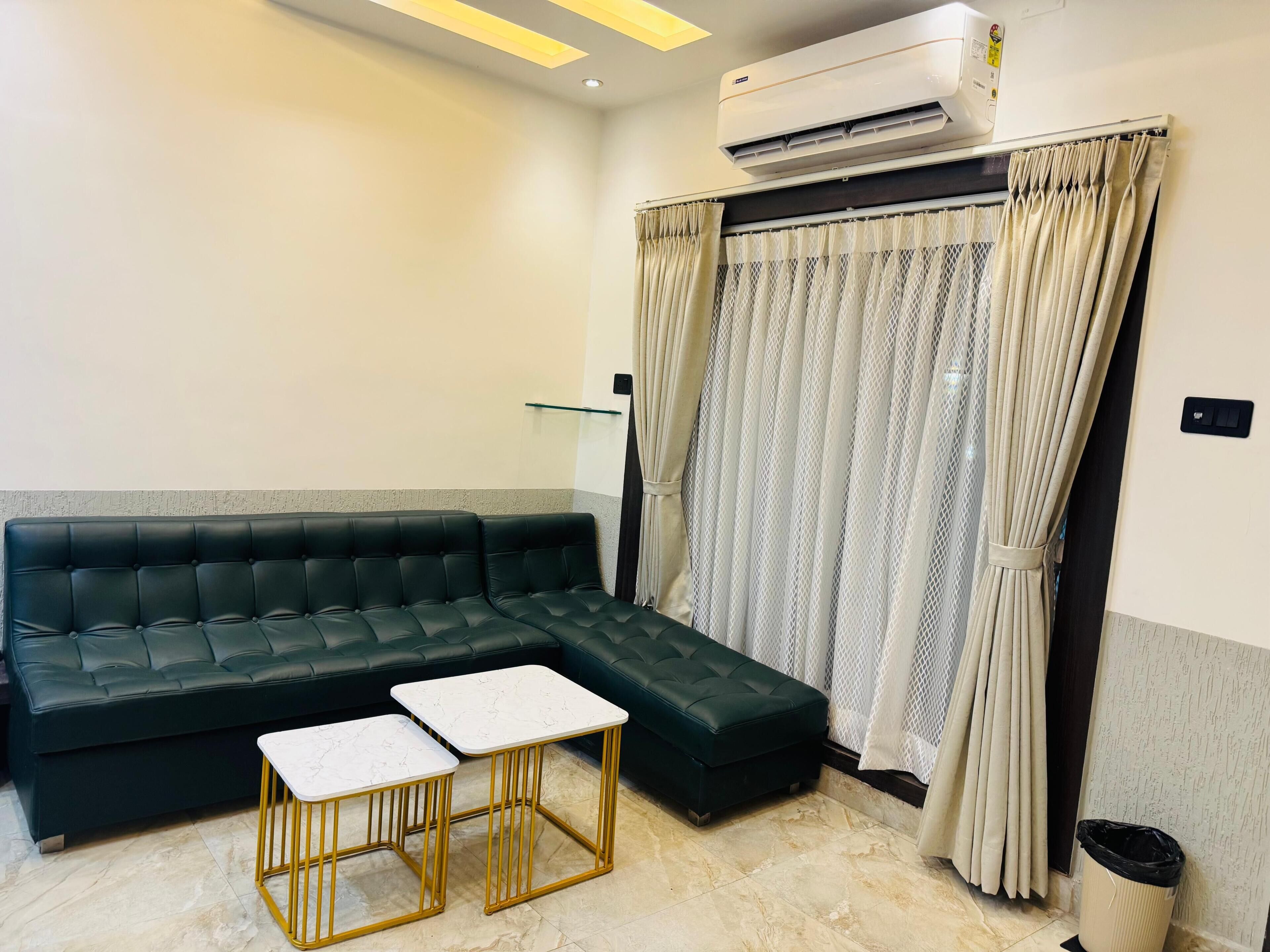 A modern living room with a sectional sofa, two small white tables, a ceiling air conditioner, and a window with curtains.