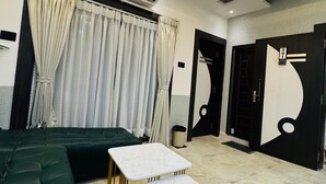 A modern hotel room with a sectional sofa, two marble-topped tables, an air conditioning unit, and a unique black and white wall design. - Ramatva Stays (Varanasi)