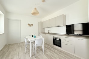 A modern kitchen with white cabinets, a black oven, a dining table with chairs, and a hanging light fixture. - S358 - Sirolo, studio apartment with garden and parking (Sirolo)