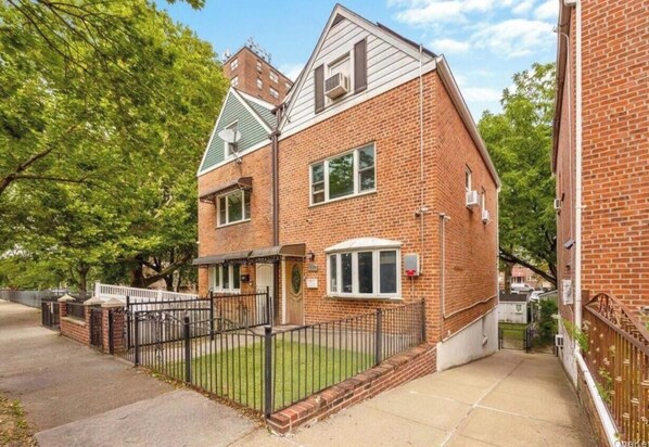 Een tweelaags bakstenen huis met voortuin, een hekpoort en een klein portaal.