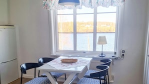 A dining area with a table, chairs, a lamp, and a view of a body of water through a window. - 3 Person Holiday Home in Bengtsfors (Bengtsfors)