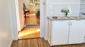 A kitchen with white cabinets, a wooden floor, a window with a red blind, and a plant on the counter. - 3 Person Holiday Home in Bengtsfors (Bengtsfors)