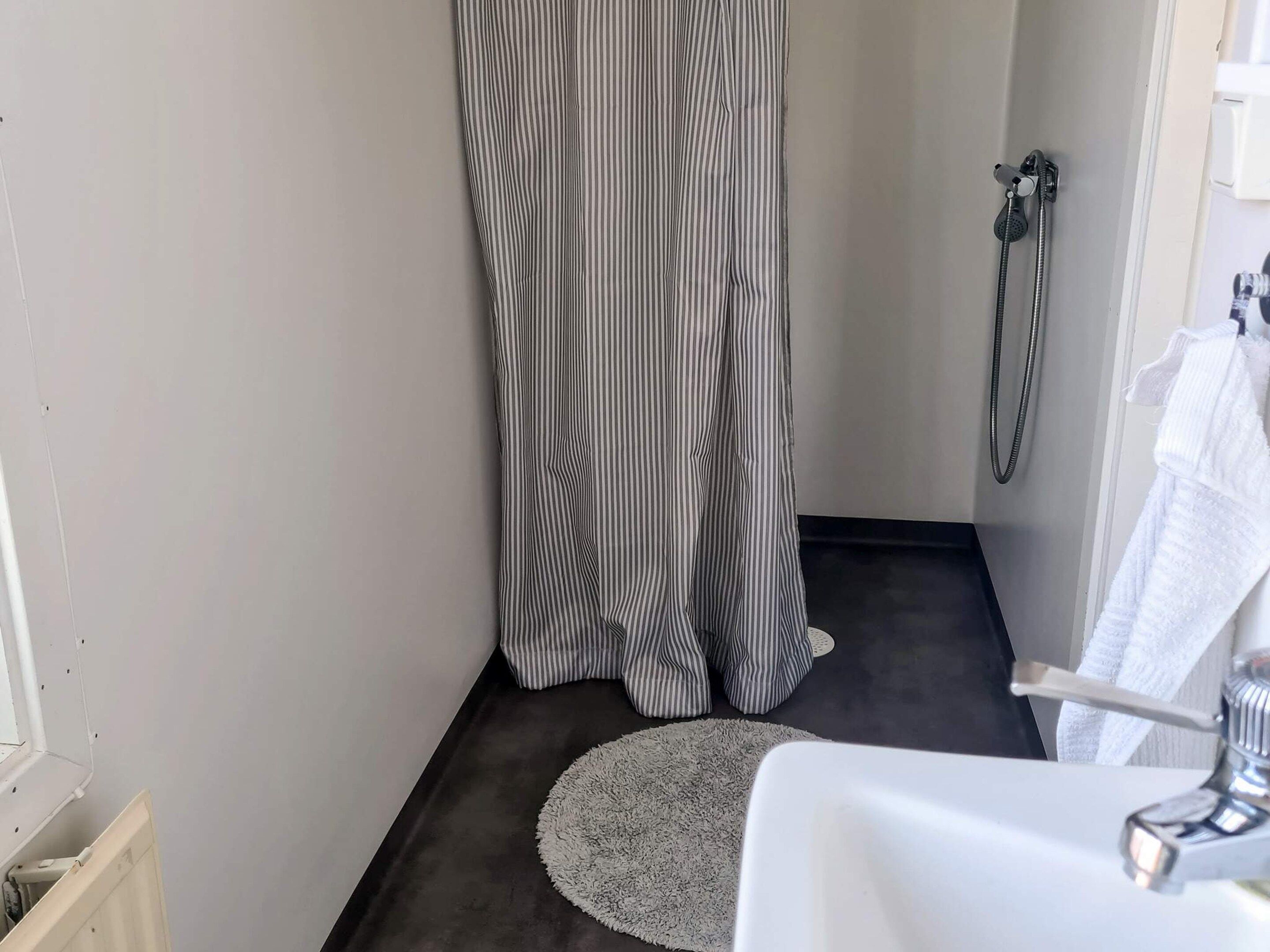 Un baño con ducha, lavamanos y un perchero para toallas.