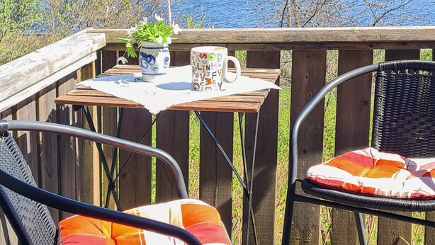 A wooden deck with a table, two chairs, a potted plant, and a mug. - 3 Person Holiday Home in Bengtsfors (Bengtsfors)