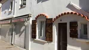 A white building with a closed shutter, a small window with wooden shutters, and a door with a metal handle. - House located on a pedestrian street leading to the beach, with private patio. (Saintes-Maries-de-la-Mer)