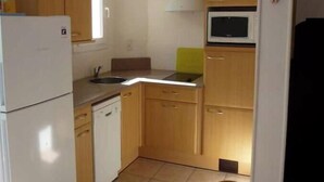A compact kitchen with a refrigerator, microwave, sink, and wooden cabinets. - House located on a pedestrian street leading to the beach, with private patio. (Saintes-Maries-de-la-Mer)