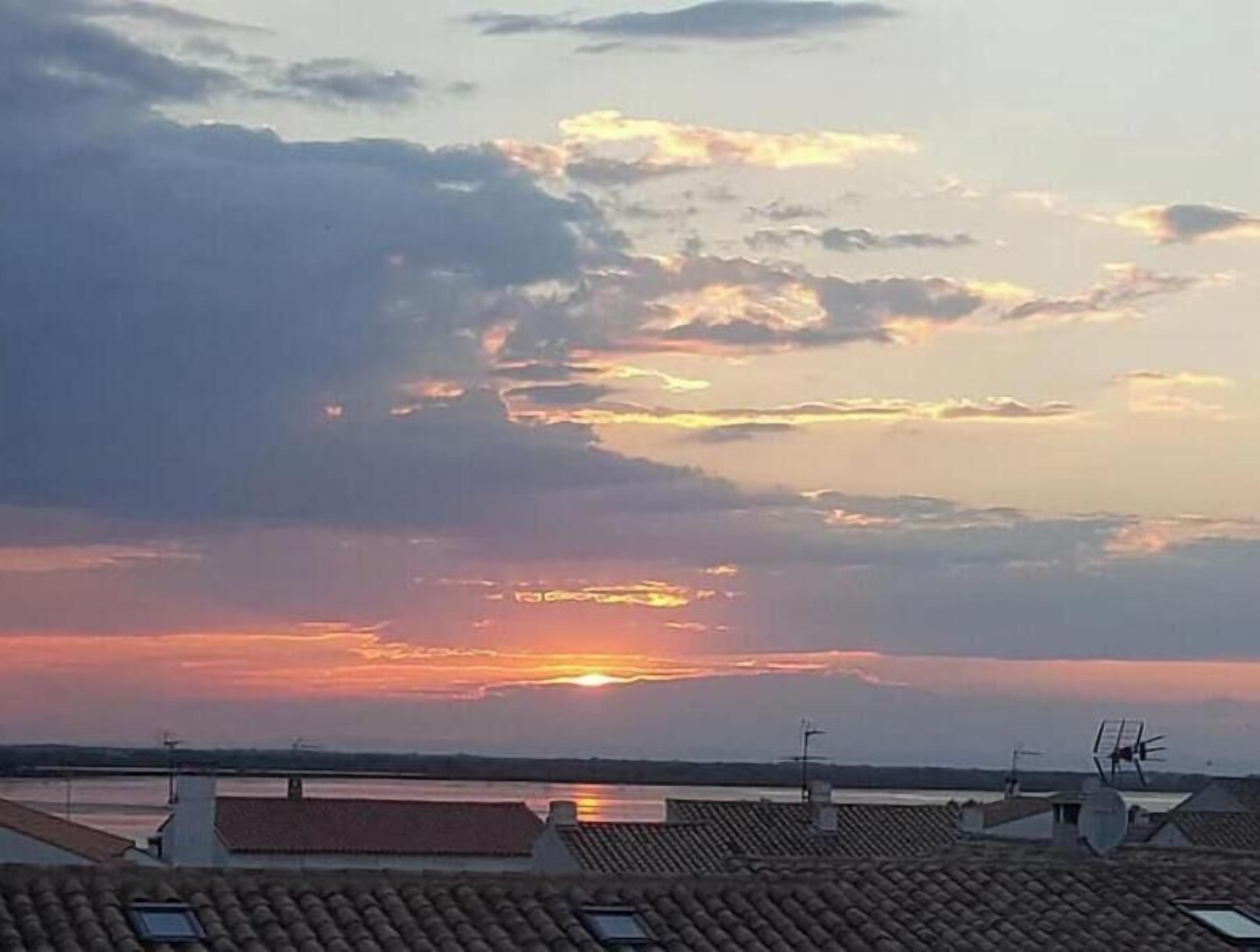 A sunset over rooftops with a body of water in the distance.