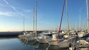 A marina with multiple boats docked, calm water, and a clear sky. - House located on a pedestrian street leading to the beach, with private patio. (Saintes-Maries-de-la-Mer)