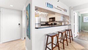 A modern kitchen with a bar area, including a refrigerator, microwave, and bar stools. - S Hampton 301 2 Br Oceanview in Kingston, Pool (Myrtle Beach)