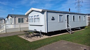 A mobile home with a front porch, a small table, and a chair. - Spacious 3-Room Van at Birchington Vale (Birchington-on-Sea)