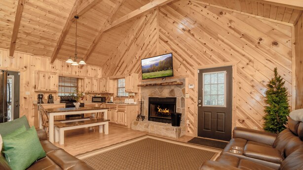 L’intérieur d’une cabane en rondins comprend une cheminée, un téléviseur fixé au-dessus, un coin repas et un espace détente avec des canapés en cuir.