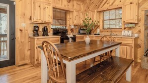 L’intérieur d’un chalet en bois comprend une cuisine équipée de meubles en bois, une table à manger avec des chaises, un poêle et un four à micro-ondes.