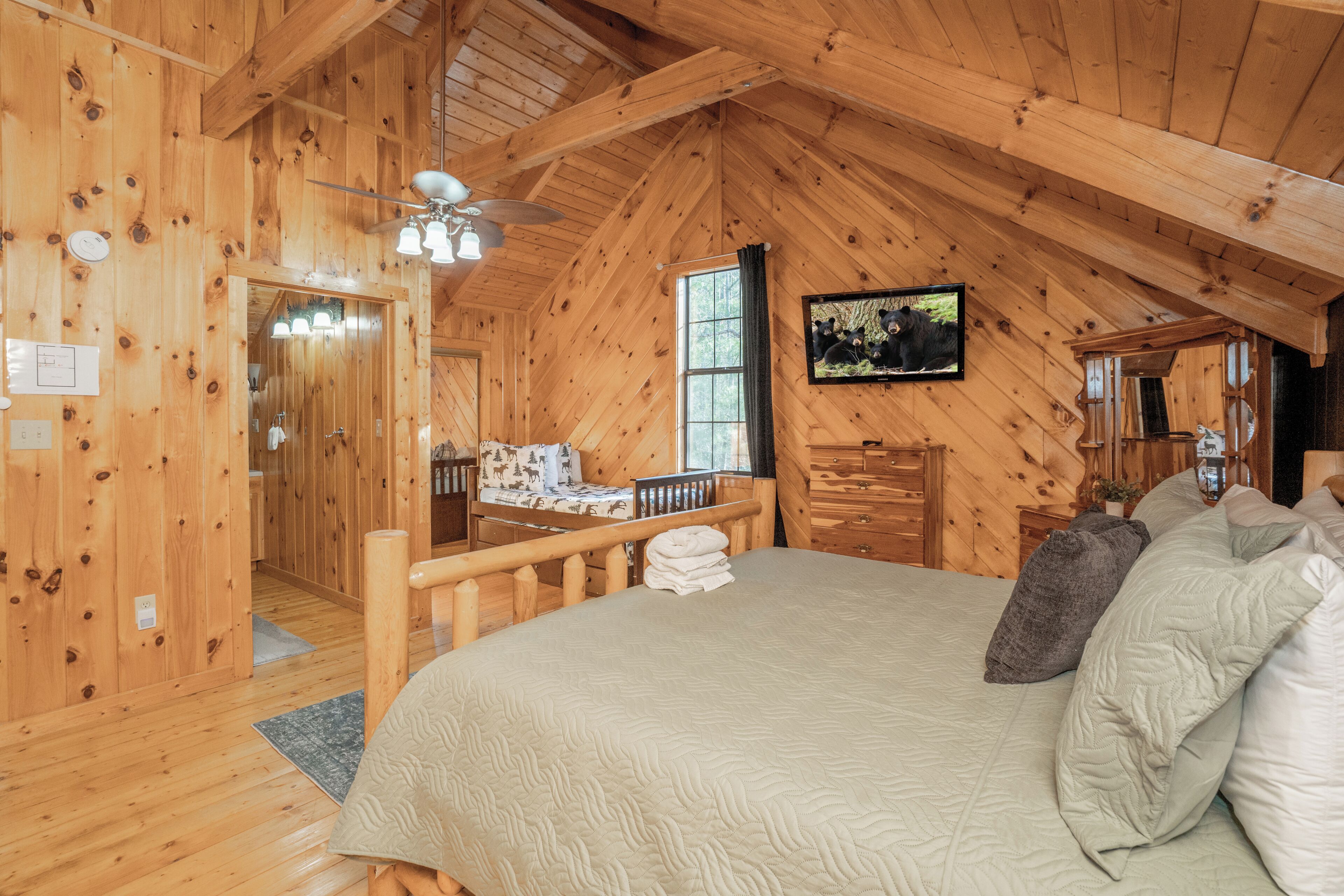 Une chambre dans une cabane en bois, avec un lit, une commode, un miroir et un ventilateur de plafond.