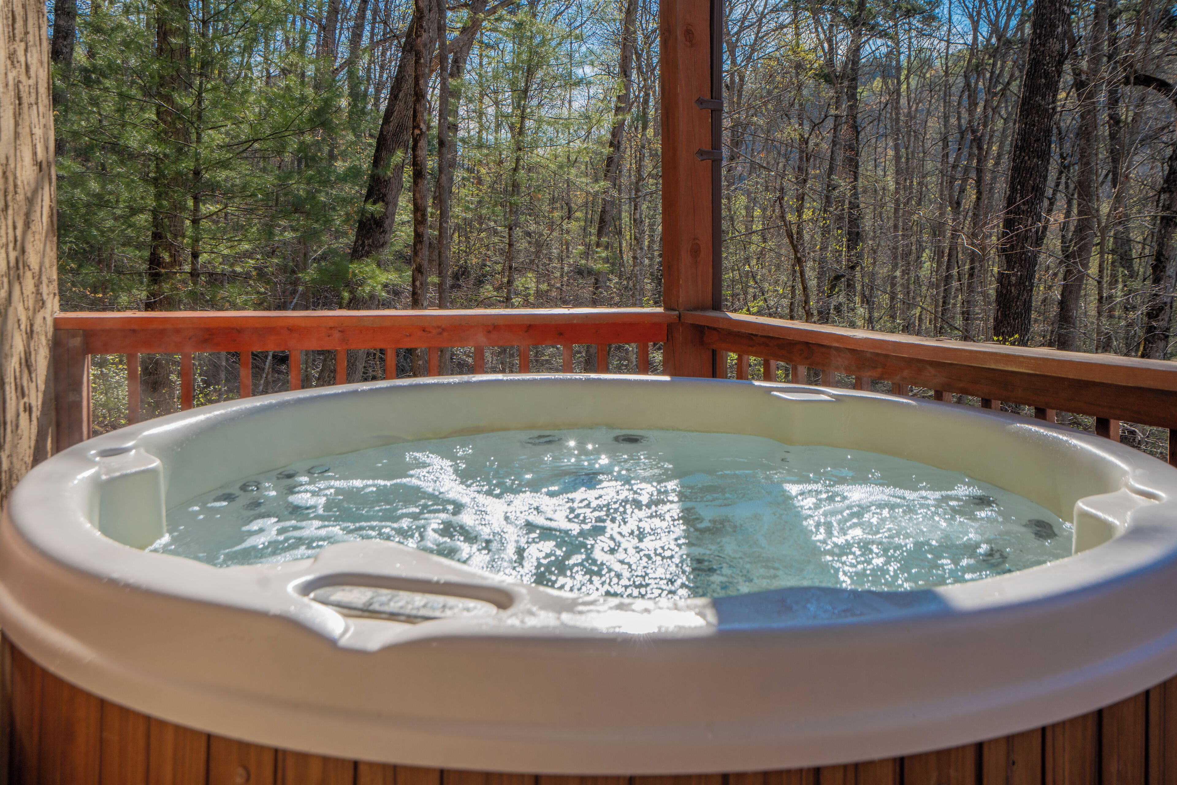 Een hottub op een houten terras met uitzicht op een bos.