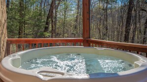 Un bain à remous sur une terrasse en bois, avec vue sur la forêt.