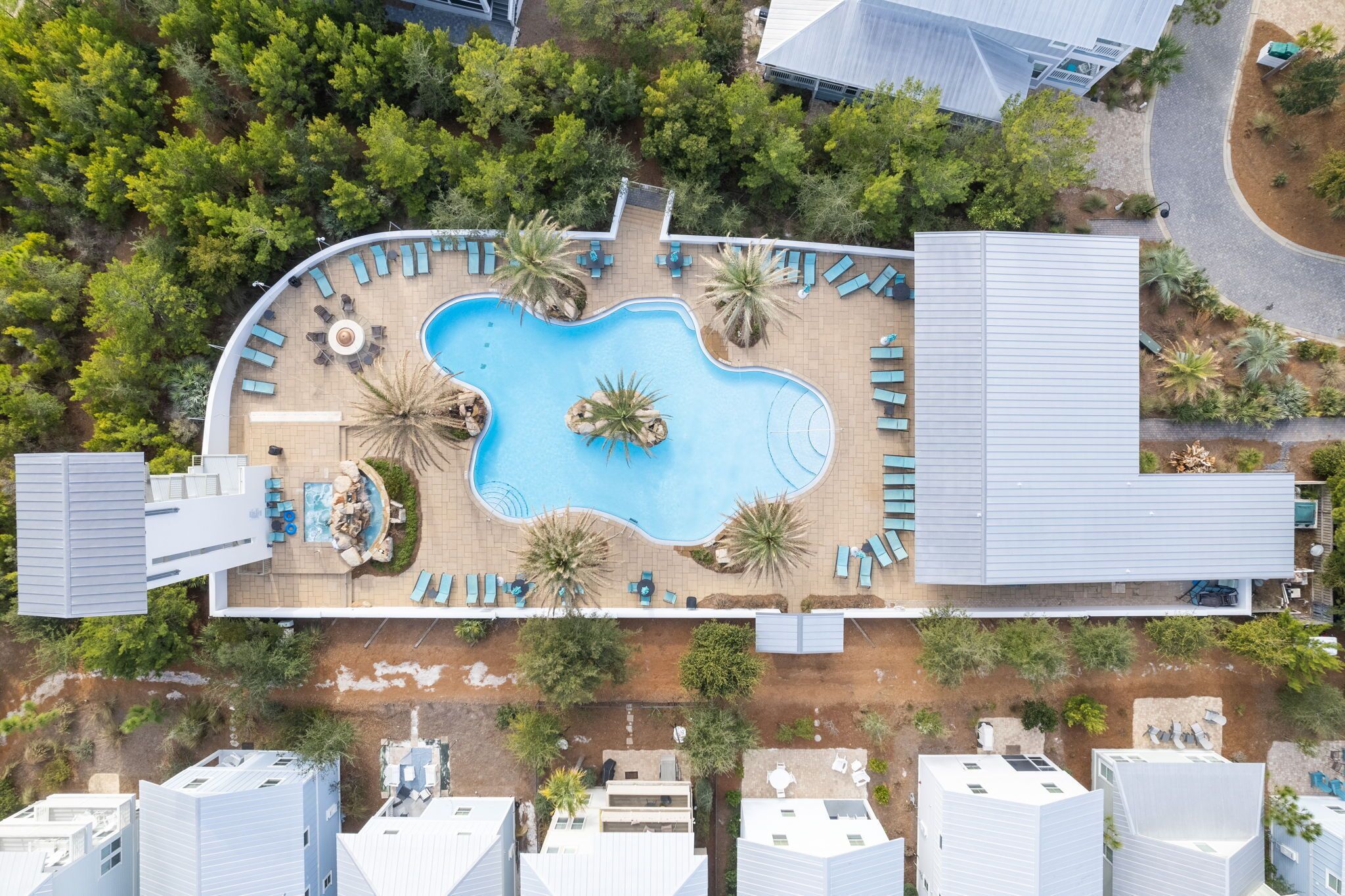 Ein Luftbild eines modernen Hotels mit einem zentral gelegenen Schwimmbad, umgeben von Liegestühlen und Palmen.