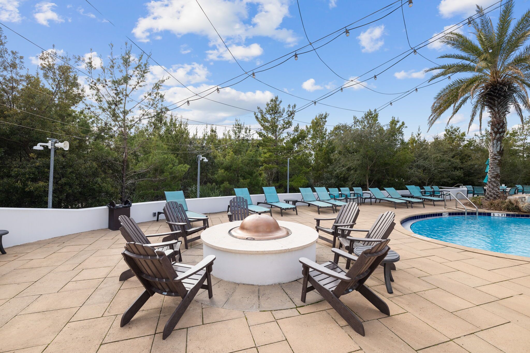 An outdoor pool area with lounge chairs and a circular seating arrangement around a central fire feature.
