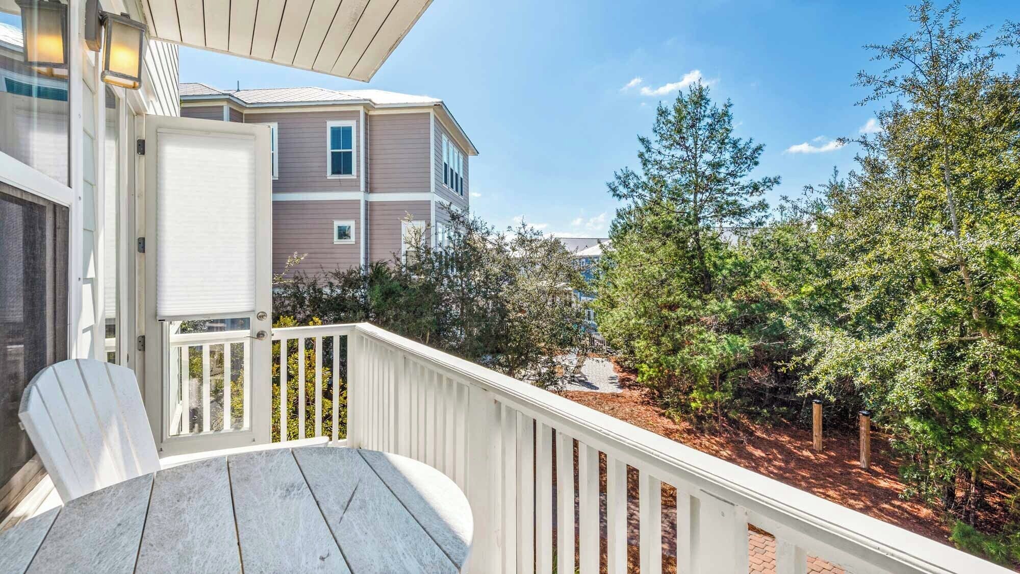 A wooden deck with a white railing, a white chair, and a view of neighboring buildings and trees.
