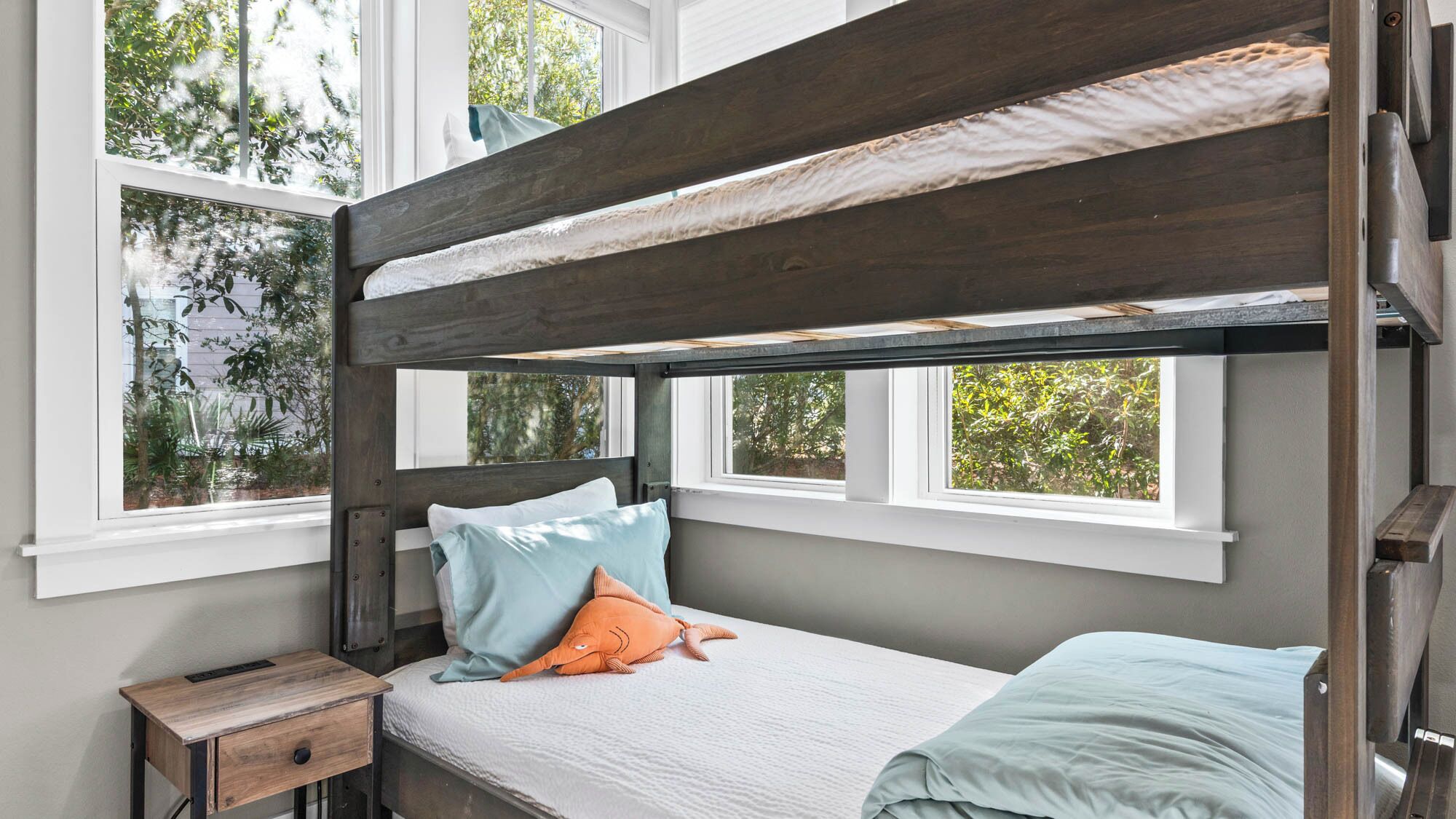 Un lit superposé avec une tête de lit en bois, une literie blanche et une petite table de chevet en bois.