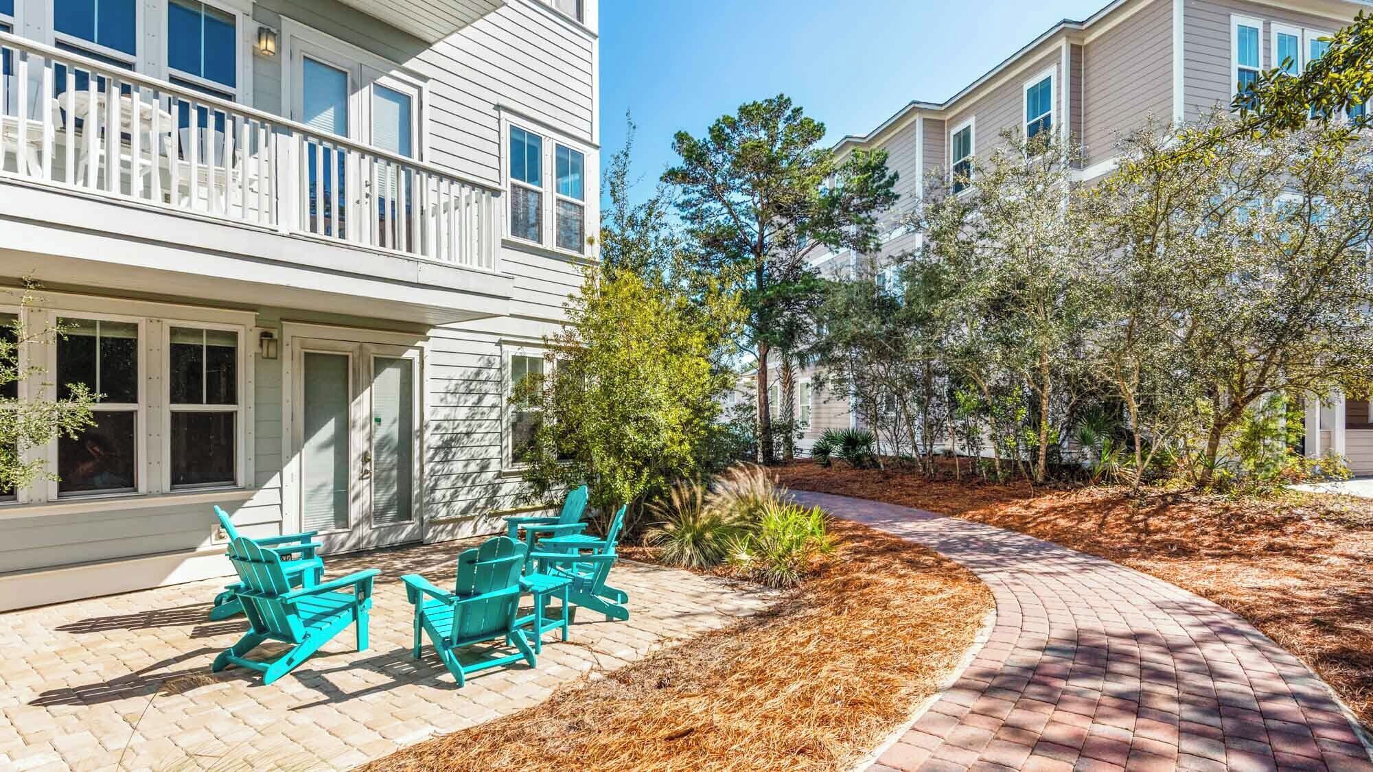 A residential building with a paved walkway, outdoor seating area, and surrounding vegetation.
