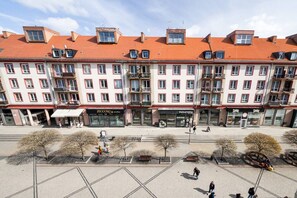 A multi-story building with a red-tiled roof, storefronts, and a paved square with trees and benches. - Świdnicka Apt - Old Town Square Nearby - by Rentujemy (Wrocław)