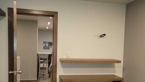 Una stanza con una panca in legno, uno sgabello, un cestino e una porta che dà su un'altra stanza.
