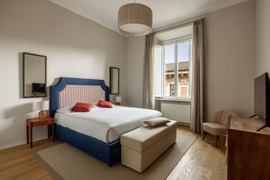 Ein Schlafzimmer mit Bett, Nachttischen, Fernseher, Fenster und Blick auf Gebäude.
