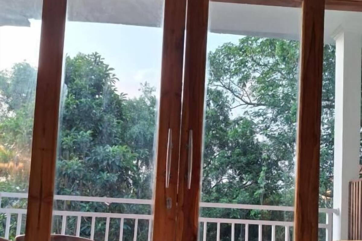 A room with a view of trees through a glass door, a white railing, and a wooden chair.