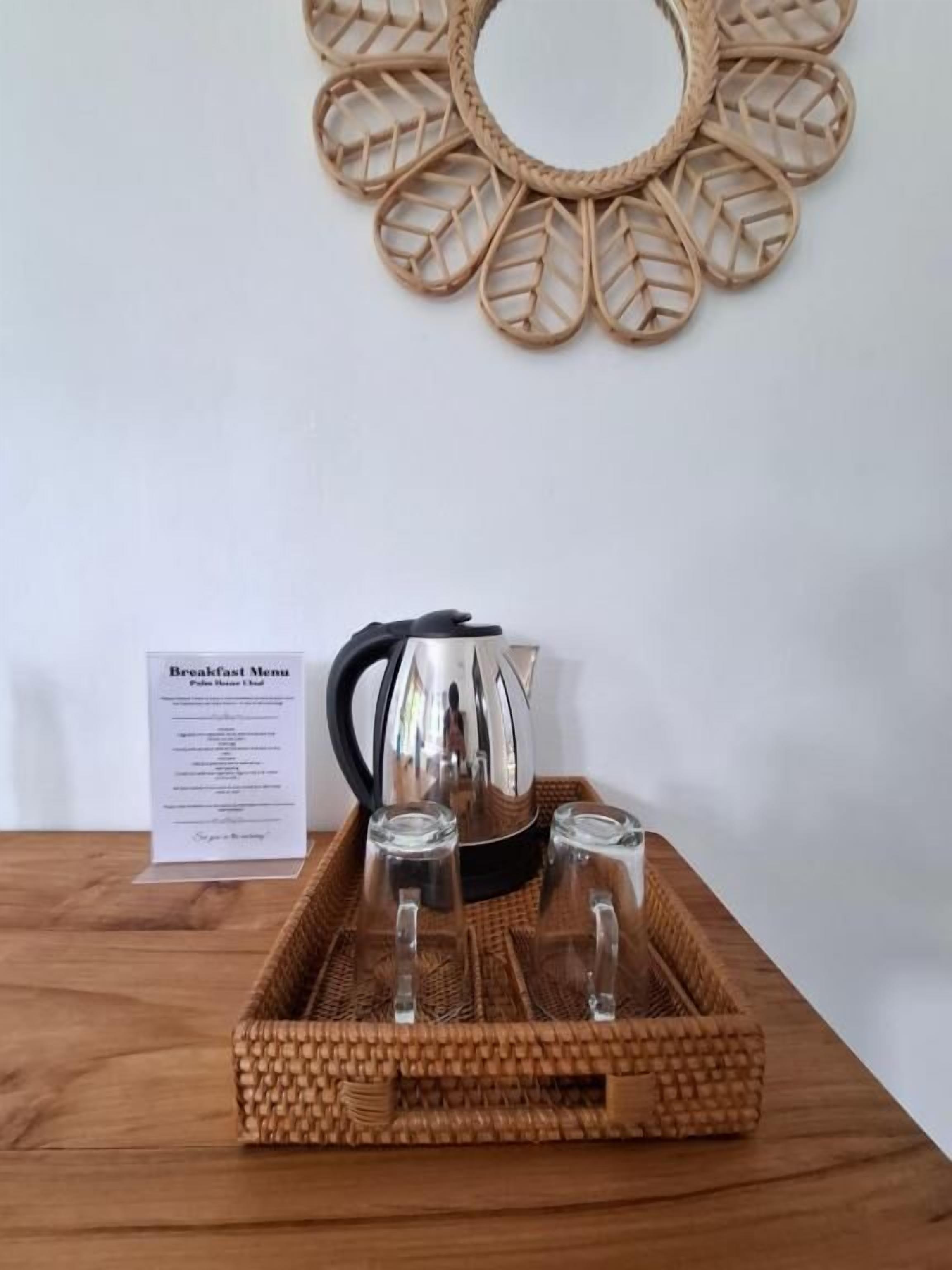 A breakfast tray with a kettle and glasses on a wooden table, a menu sign, and a woven wall decoration.