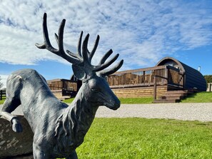 A deer sculpture in a grassy area with a wooden structure in the background. - Heather Heights (Whitby)