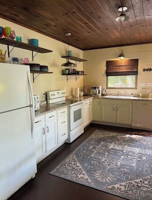 A kitchen with white cabinets, a stove, and a refrigerator. There are shelves above the counter holding various items.