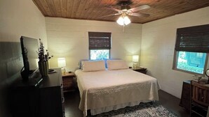 Un dormitorio con techo de madera, una cama con cubrecama blanco, una mesita de noche, un escritorio, una silla y una ventana con persianas.