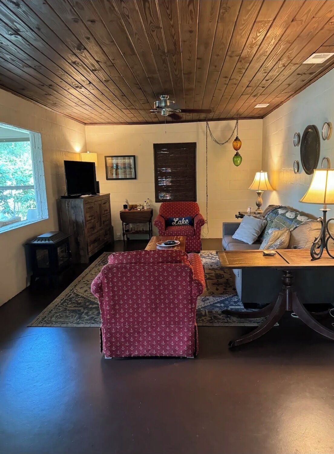 Un salon chaleureux avec un plafond en bois, un téléviseur, une cheminée et une fenêtre donnant sur les arbres.