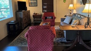 Una sala de estar acogedora, con techo de madera, televisor, chimenea y ventana con vista a árboles.