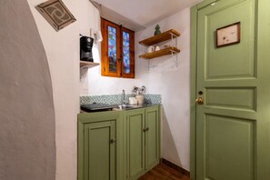 Een keuken met groene kastjes, een koffieapparaat, een raam met glas-in-lood en een deur met een klok.