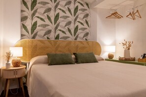 Een netjes ingerichte hotelkamer met een groot bed, twee nachtkastjes, een muur met een bladmotief en houten kledinghangers aan de wand.