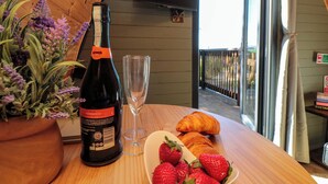 Una bottiglia di vino, un bicchiere, fragole e croissant su un tavolo di legno con vista su un balcone.