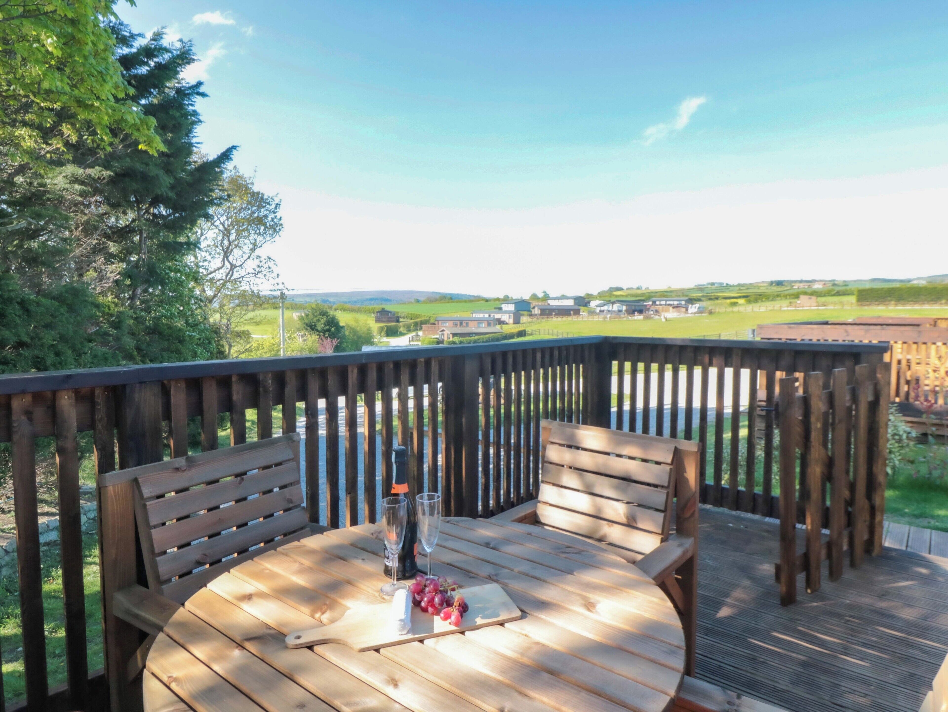 A wooden deck with a round table, two chairs, and a bottle of wine.