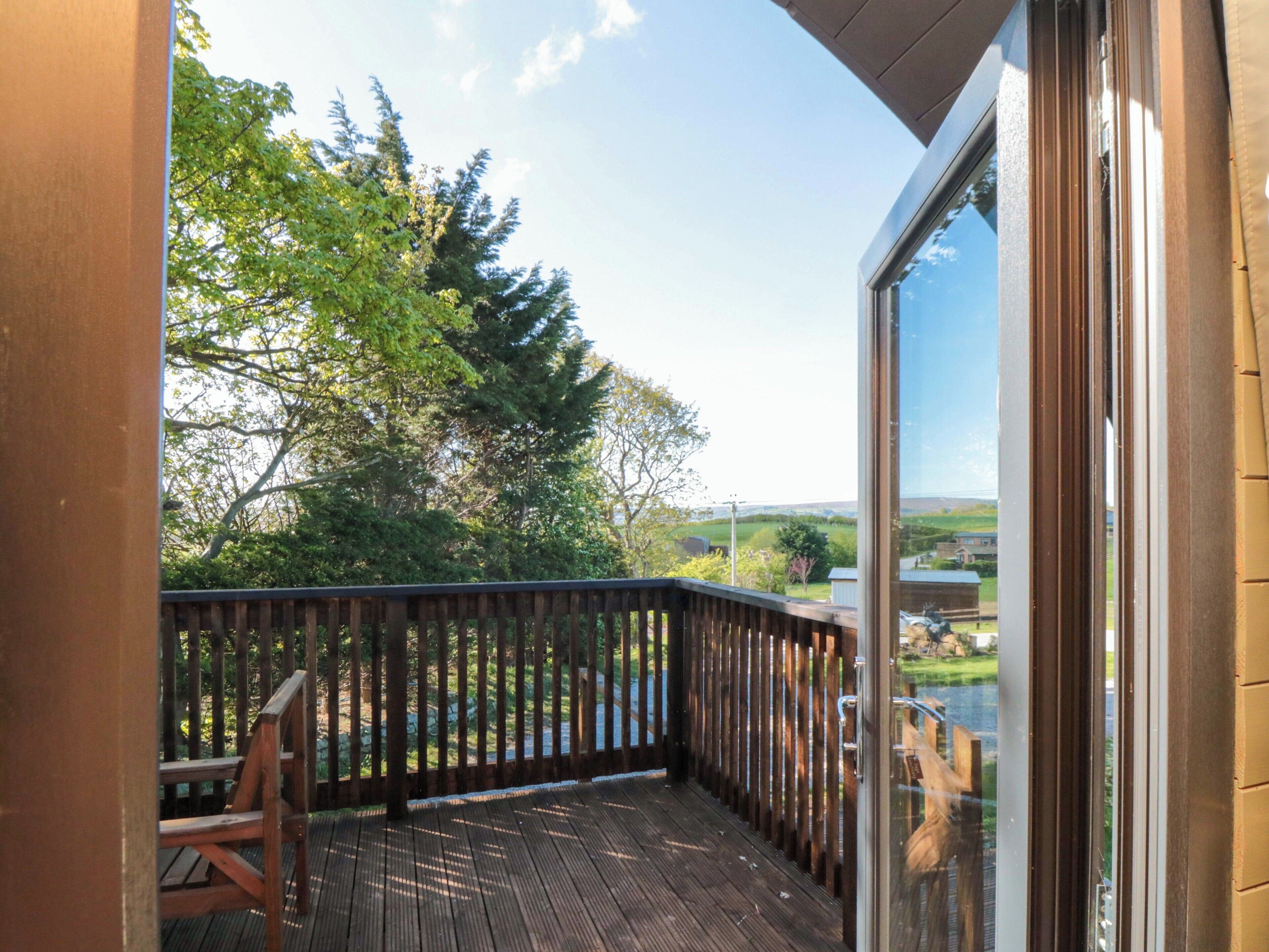 Eine Holzterrasse mit Glastür und Blick auf Bäume und Hügel.