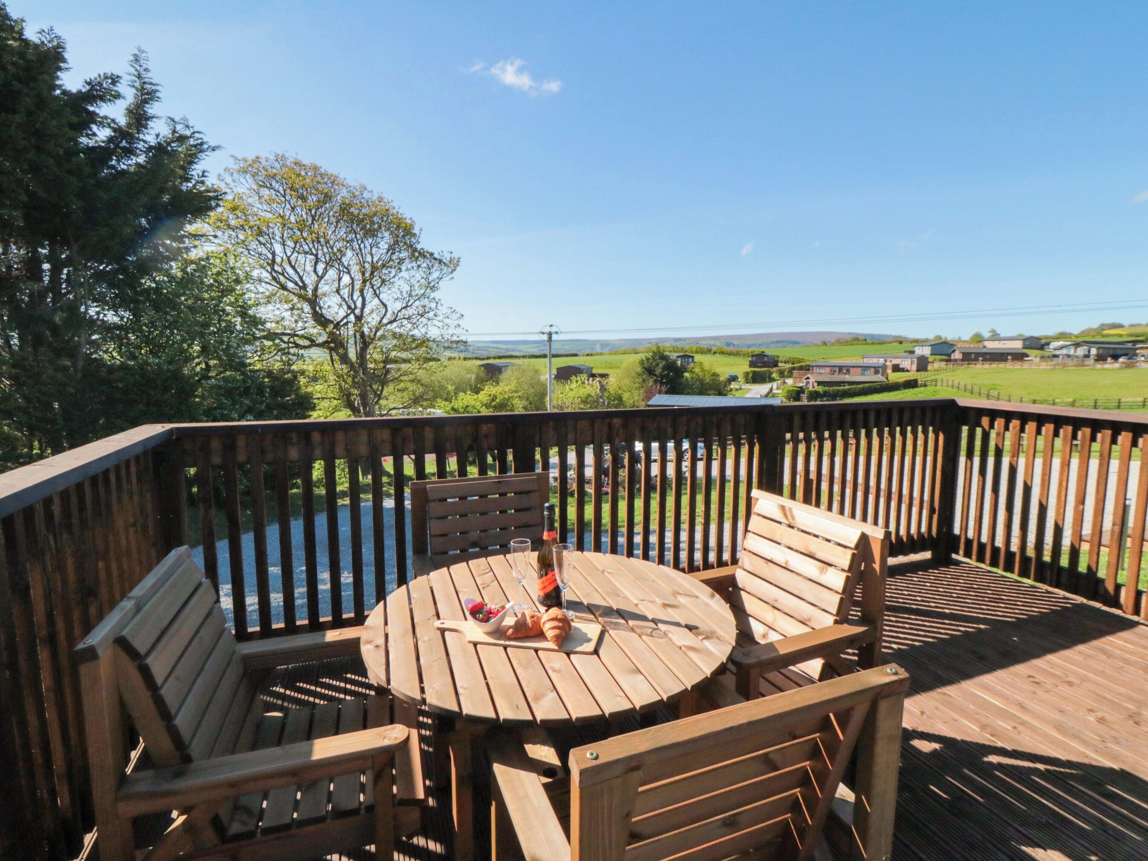 A wooden deck with a round table and two chairs, overlooking a scenic landscape.
