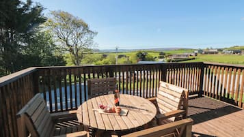 A wooden deck with a round table and two chairs, overlooking a scenic landscape.