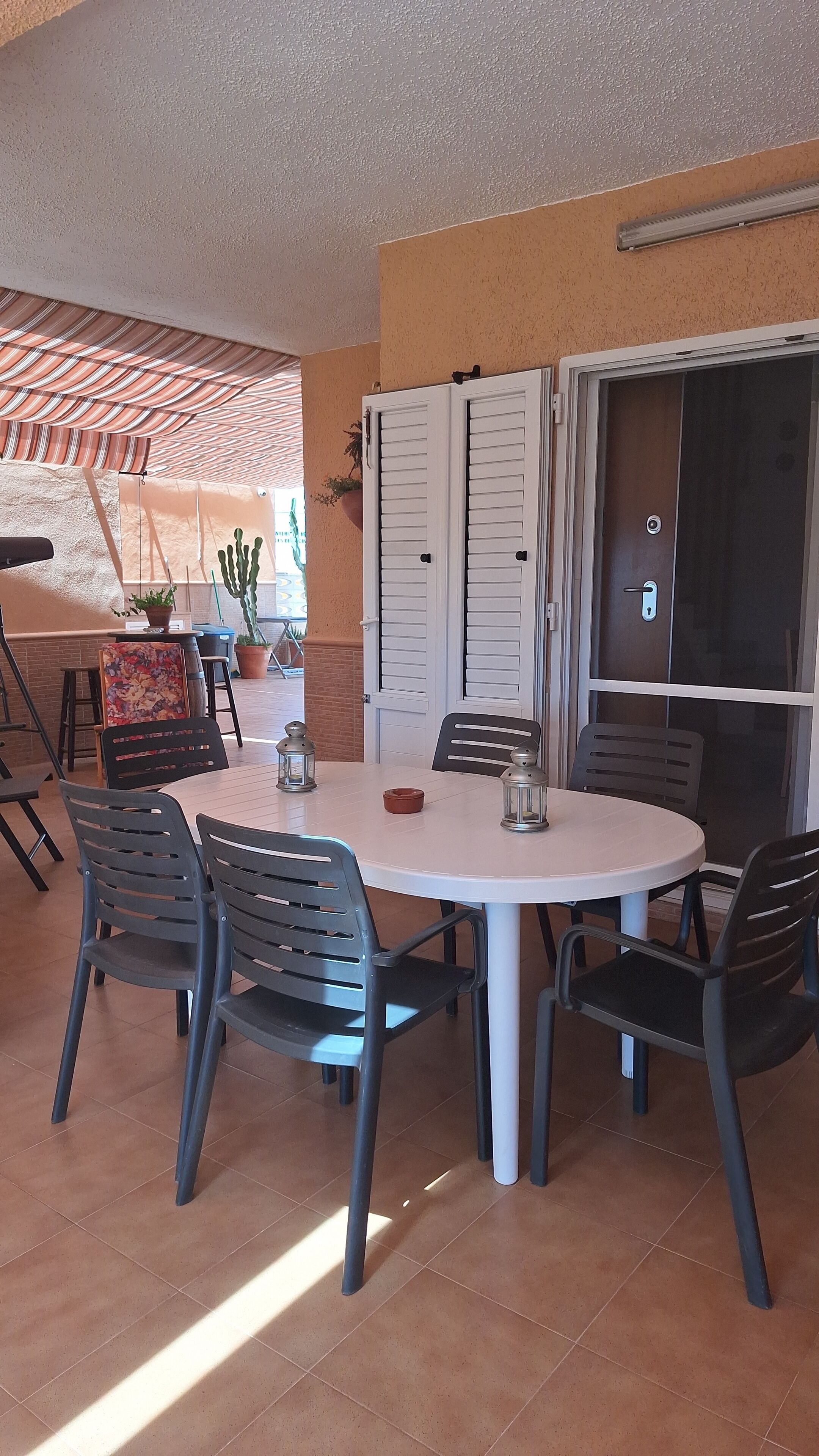 Una mesa redonda para comer con seis sillas, una planta en maceta y una puerta con ventana corredera de vidrio.