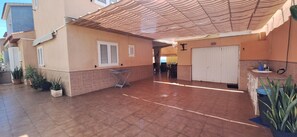 Ein überdachter Patio-Bereich mit Fliesenböden, einer weißen Tür und Topfpflanzen.
