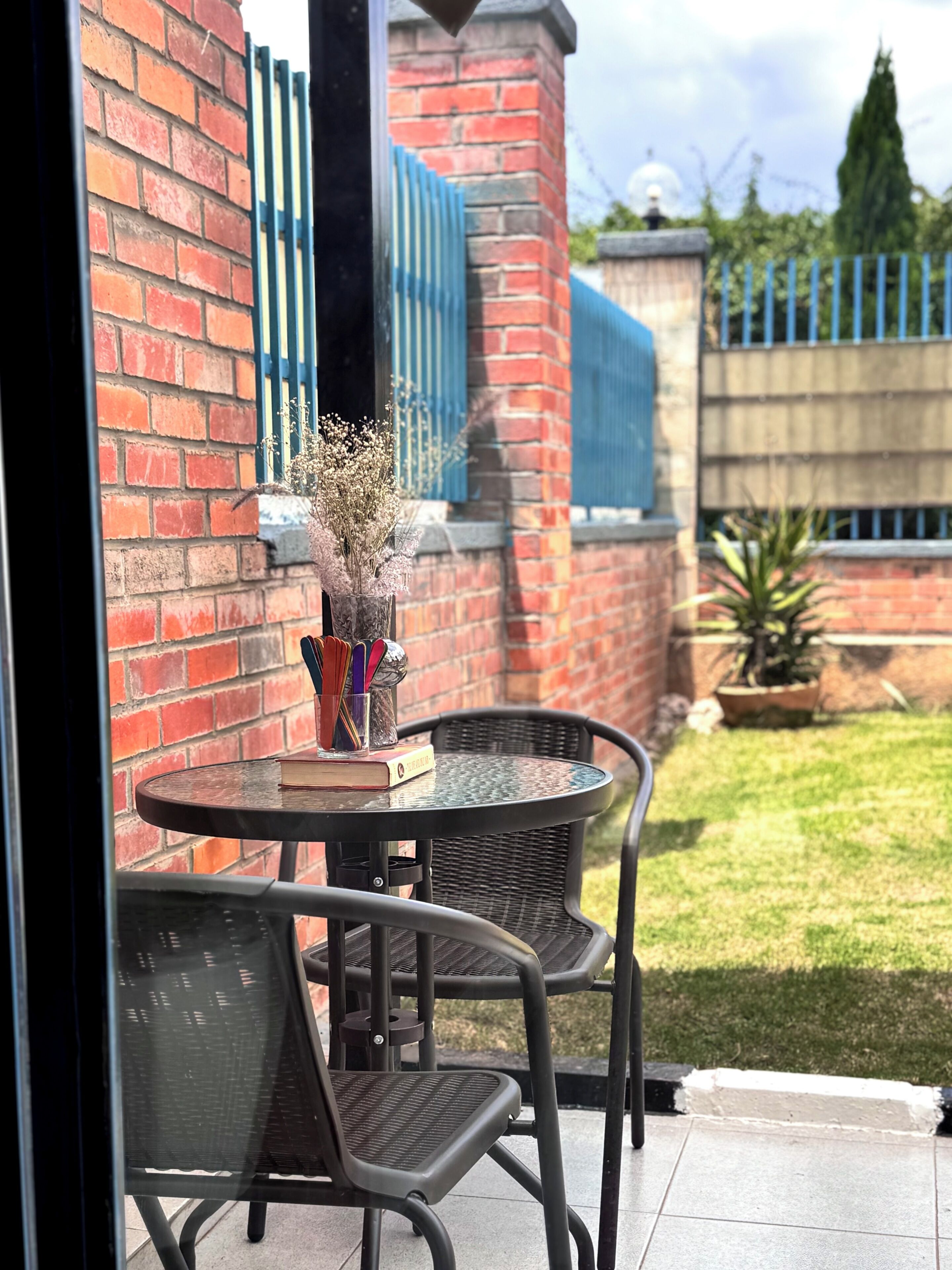 A patio area with a round table and two chairs, a vase with dried flowers, and a book.