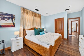 Une chambre à coucher avec un lit en bois, une table de chevet, une lampe, un tableau et une porte donnant sur une autre pièce.