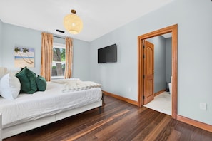 Ein Schlafzimmer mit Bett, Fernseher, Fenster mit Vorhängen, Tür und Deckenleuchte.