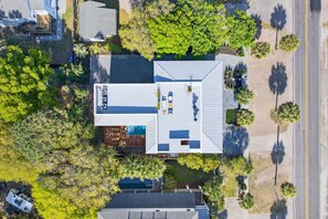 An aerial view of a modern house with a large deck, a swimming pool, and a well-maintained garden. - 7 Bedroom Oceanview home with Pool | Rooftop Deck | Across Street From Beach (Isle of Palms)