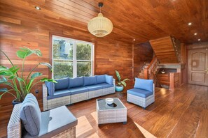 A wooden interior with a sofa, two chairs, a coffee table, a hanging light fixture, and a staircase. - 7 Bedroom Oceanview home with Pool | Rooftop Deck | Across Street From Beach (Isle of Palms)