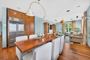 Eine moderne Küche mit Holzschränken, einem Edelstahlkühlschrank und einem Essbereich mit Holztisch und weißen Stühlen.