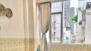 Una habitación con cama, una mesita, una ventana con cortinas y papel tapiz estampado.